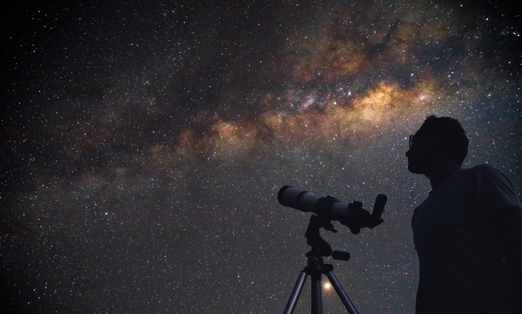 Photo of a man looking at the night sky with a telescope